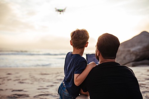 Father and son flying drone at the beach